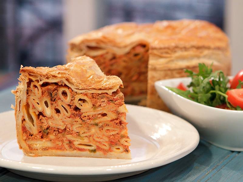 Una rodaja de timpana en un plato delante de un bol de ensalada y la timpana restante