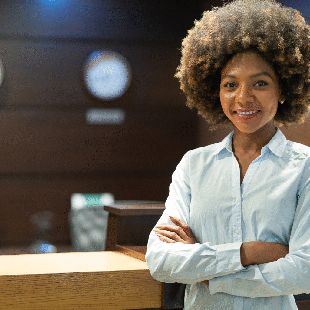 Camarera sonriente y confiada con los brazos cruzados, reflejando el espíritu acogedor y profesional del sector de hostelería en Malta.
