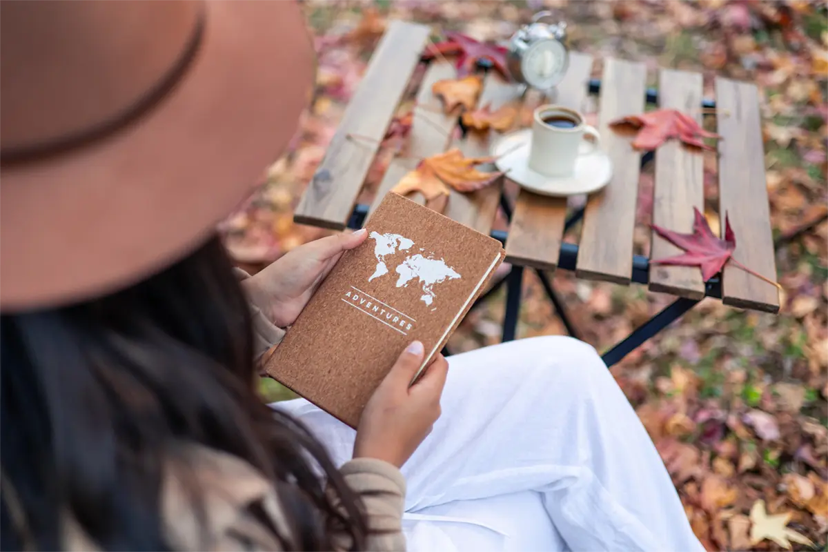 Chica sujetando un cuaderno con un café