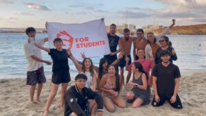 Grupo de estudiantes disfrutando en la playa con la bandera de Malta for Students, representando la comunidad que marca la diferencia al estudiar inglés en Malta.