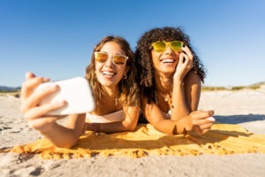 Dos jóvenes estudiantes tomando el sol en la playa de Malta, sonriendo y disfrutando del buen tiempo en verano