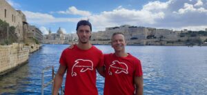 Instructores de buceo posando frente al mar en Malta, con la ciudad de La Valeta al fondo durante la experiencia de buceo de Malta for Students