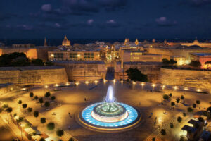 Vista nocturna de La Valeta, Malta, con la Fuente de Tritón iluminada y las murallas de la ciudad al fondo. Imagen representativa de qué ver en La Valeta al anochecer.